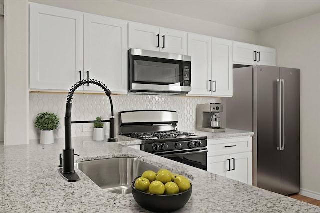 kitchen featuring light stone counters, stainless steel appliances, backsplash, white cabinetry, and a sink