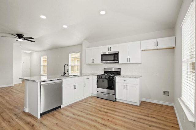 kitchen with appliances with stainless steel finishes, white cabinets, a sink, and a peninsula