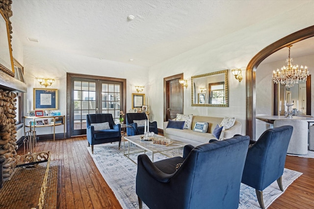 living area with arched walkways, hardwood / wood-style flooring, an inviting chandelier, a textured ceiling, and french doors