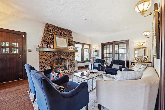 living area featuring an inviting chandelier, a stone fireplace, a textured ceiling, and wood finished floors