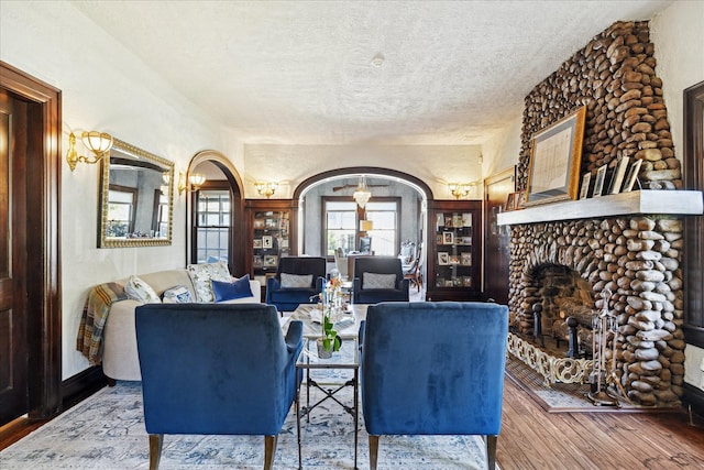 living area featuring wood finished floors, a fireplace with raised hearth, a textured ceiling, a chandelier, and arched walkways