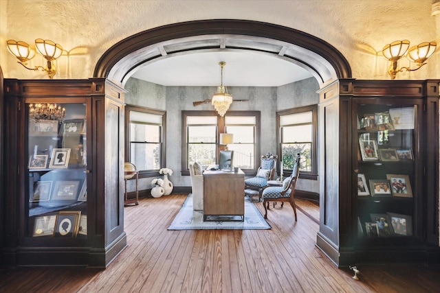 office area with arched walkways, wood-type flooring, and baseboards