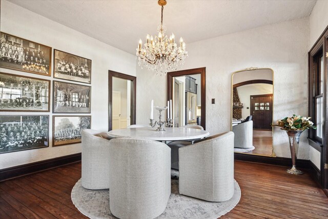 dining space with arched walkways, a notable chandelier, dark wood finished floors, and baseboards