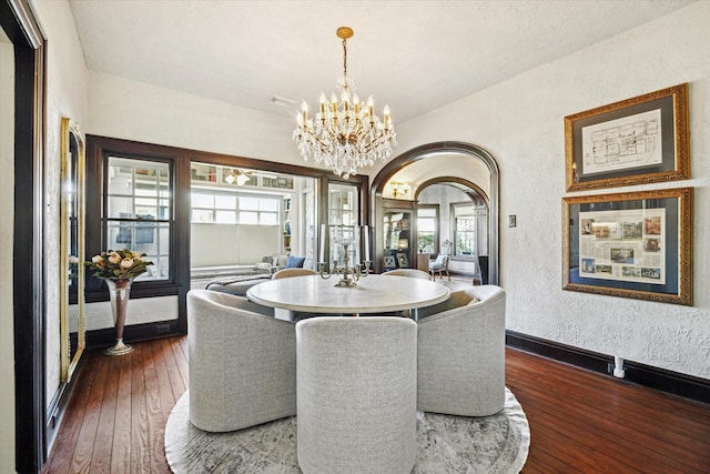 dining space featuring a textured wall, arched walkways, a chandelier, baseboards, and hardwood / wood-style flooring