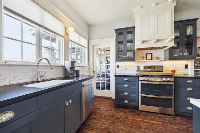 kitchen with appliances with stainless steel finishes, dark countertops, dark wood-style flooring, and a sink