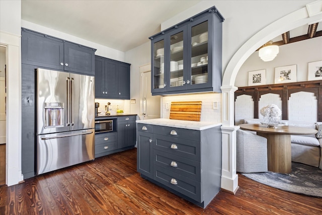 kitchen featuring built in microwave, high quality fridge, light countertops, glass insert cabinets, and dark wood-type flooring