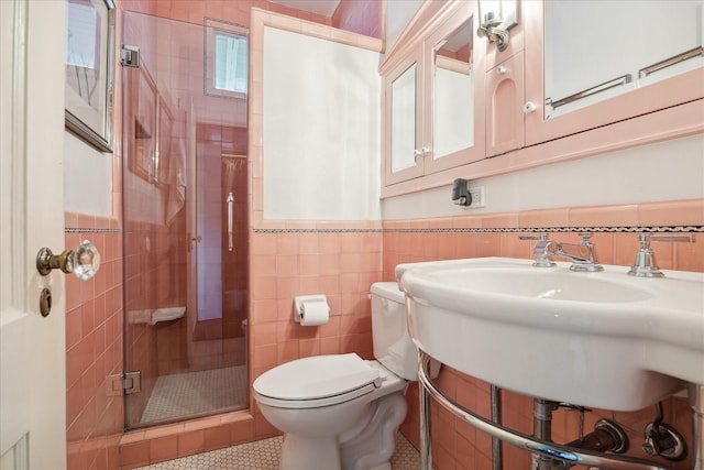 full bathroom with a stall shower, tile walls, toilet, tile patterned floors, and a sink