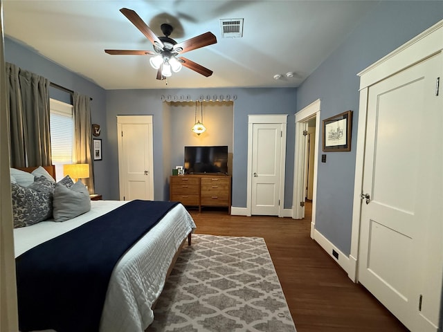 bedroom with ceiling fan, dark wood-style flooring, visible vents, baseboards, and multiple closets