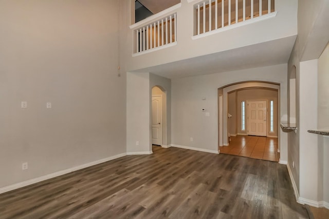 empty room featuring baseboards, a high ceiling, arched walkways, and wood finished floors