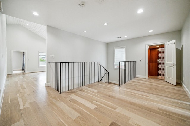 empty room featuring lofted ceiling, light wood-type flooring, and plenty of natural light