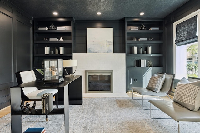 interior space featuring a textured ceiling, a decorative wall, recessed lighting, built in features, and a glass covered fireplace