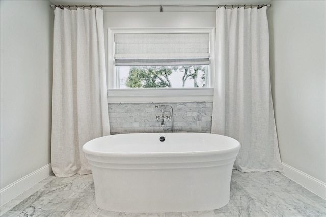 full bathroom featuring marble finish floor, baseboards, and a freestanding tub