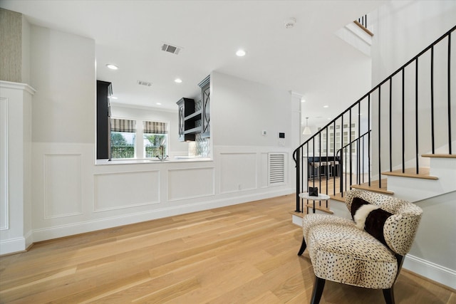 living area with a wainscoted wall, recessed lighting, visible vents, stairway, and light wood-style flooring