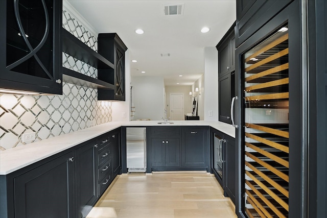 bar featuring wine cooler, light wood-style flooring, a sink, visible vents, and backsplash