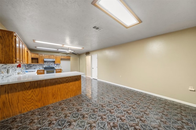 kitchen featuring a peninsula, a textured ceiling, stainless steel electric range, visible vents, and brown cabinetry