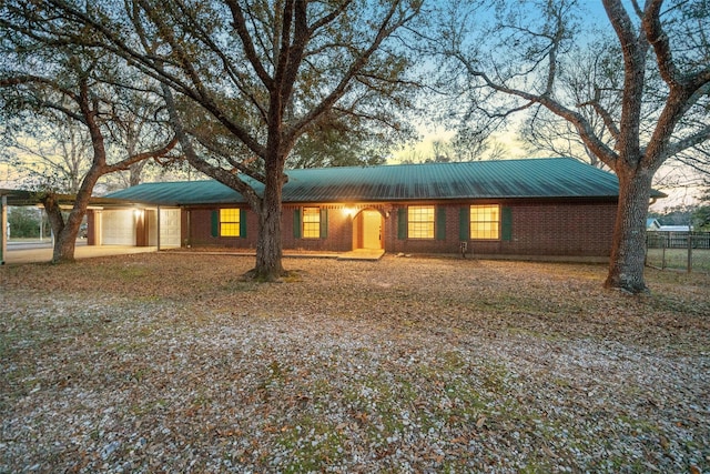 ranch-style home featuring an attached garage, fence, metal roof, and brick siding