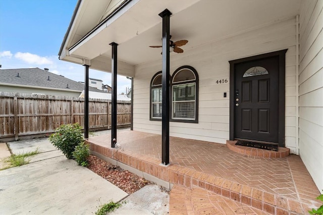 view of exterior entry featuring covered porch, fence, and ceiling fan