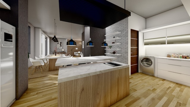 kitchen featuring washer / clothes dryer, hanging light fixtures, and light wood-style flooring