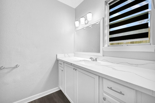 bathroom featuring a textured wall, vanity, baseboards, and wood finished floors