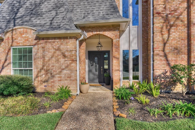 entrance to property with a shingled roof, brick siding, and mansard roof