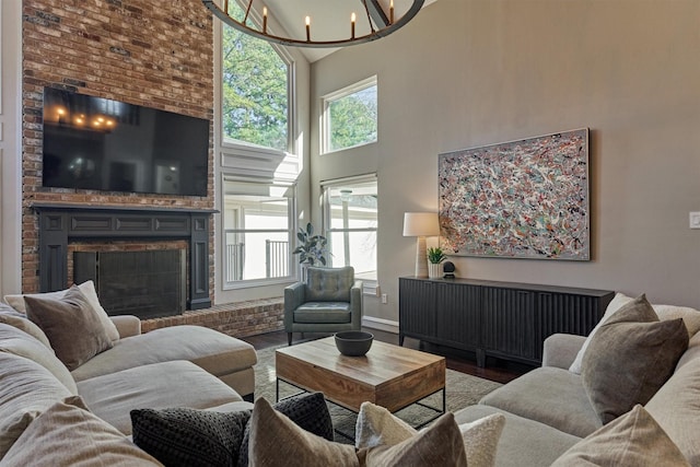 living area with a notable chandelier, wood finished floors, a towering ceiling, baseboards, and a brick fireplace