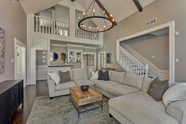 living room featuring visible vents, dark wood-style flooring, beamed ceiling, stairs, and a chandelier