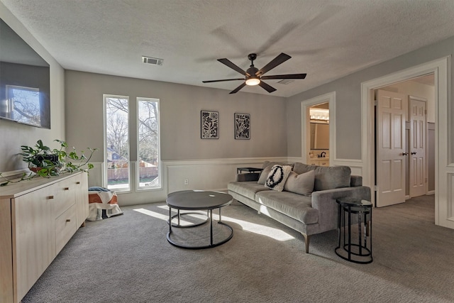 living room with a wainscoted wall, carpet floors, a textured ceiling, and visible vents