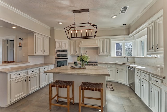 kitchen featuring visible vents, a kitchen island, a kitchen breakfast bar, stainless steel appliances, and a sink