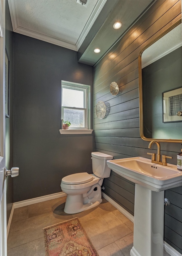 half bath with visible vents, baseboards, toilet, tile patterned floors, and crown molding