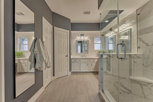 full bathroom with vanity, a marble finish shower, and visible vents