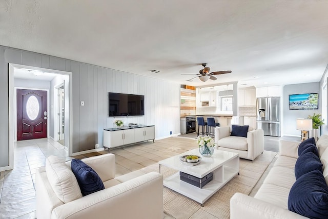 living room with baseboards, visible vents, and a ceiling fan