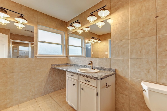 bathroom with toilet, vanity, tile walls, a tile shower, and tile patterned floors