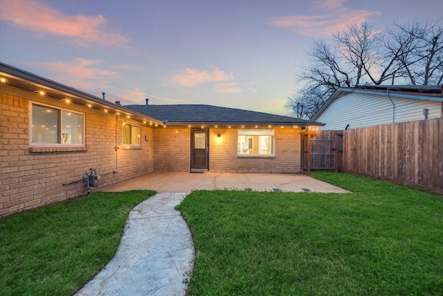 back of property at dusk featuring a patio area, brick siding, fence, and a lawn