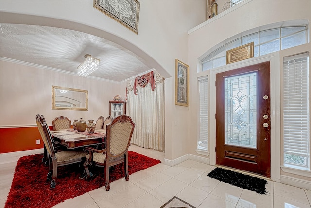 foyer entrance with ornamental molding, arched walkways, baseboards, and light tile patterned floors