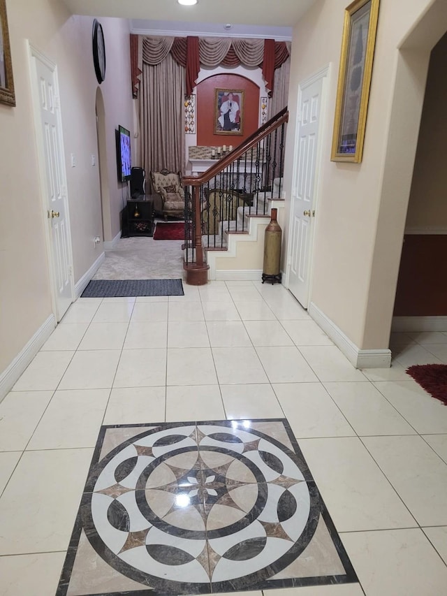 entryway featuring light tile patterned floors, baseboards, stairway, and arched walkways