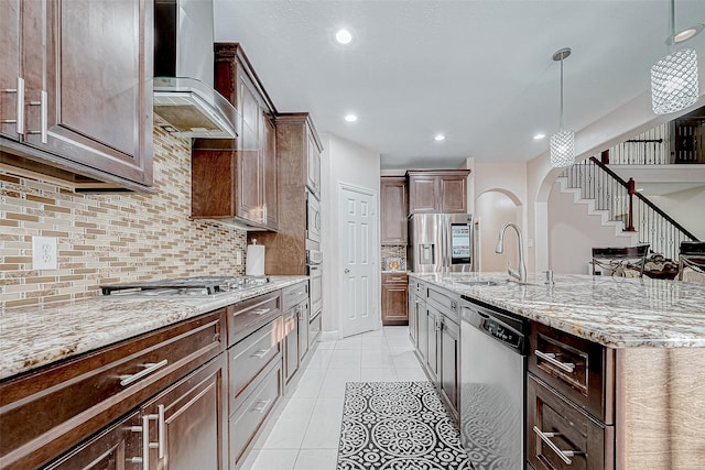 kitchen with arched walkways, light tile patterned floors, a sink, appliances with stainless steel finishes, and wall chimney exhaust hood