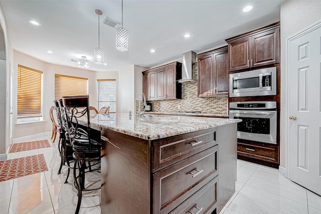 kitchen with wall chimney exhaust hood, appliances with stainless steel finishes, a sink, and light tile patterned flooring