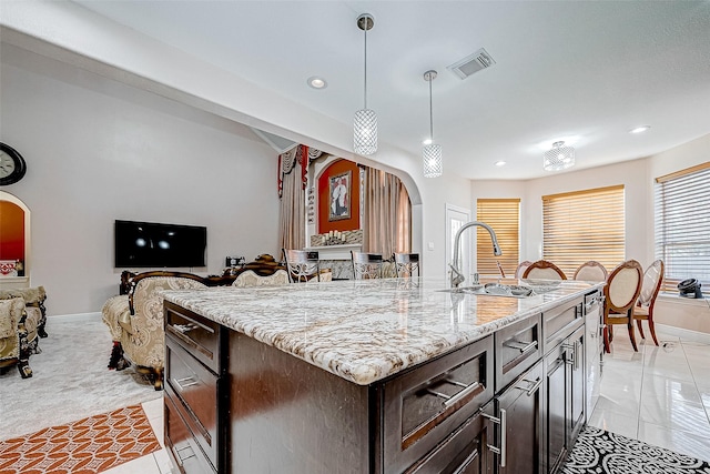 kitchen featuring visible vents, arched walkways, decorative light fixtures, light stone countertops, and a sink