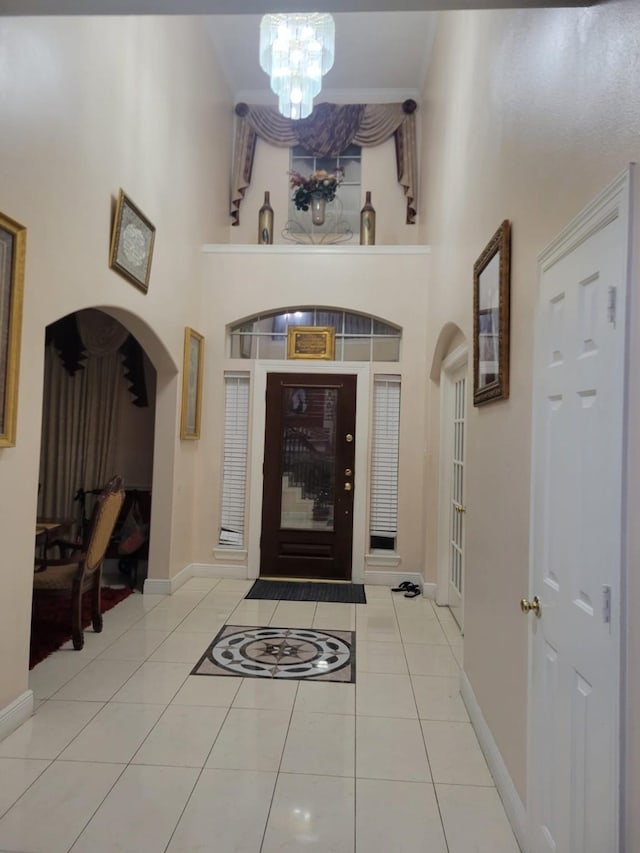 foyer with arched walkways, a high ceiling, baseboards, and tile patterned floors