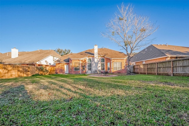 rear view of house featuring brick siding, a yard, a chimney, a patio area, and a fenced backyard