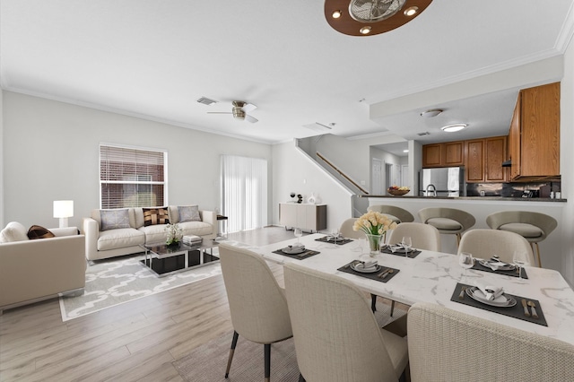 dining space with light wood-style flooring, visible vents, ornamental molding, and ceiling fan