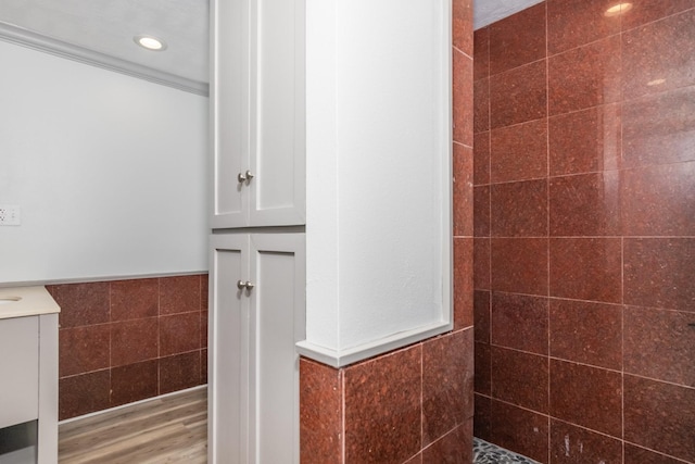 bathroom featuring tile walls, wainscoting, vanity, wood finished floors, and tiled shower