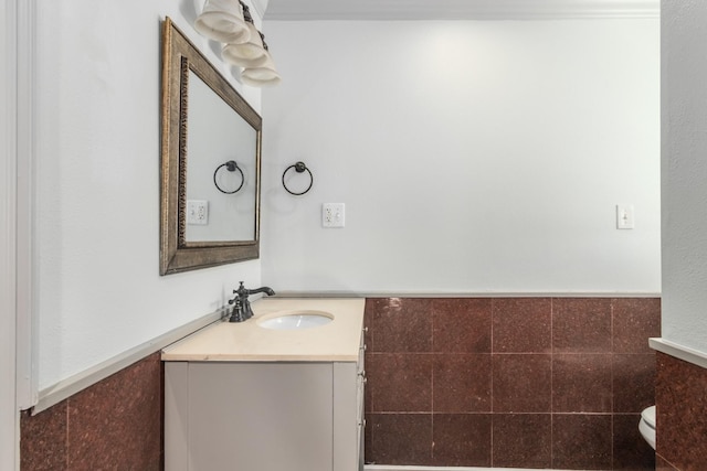 half bath with toilet, wainscoting, tile walls, and vanity