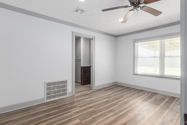 empty room featuring visible vents, crown molding, baseboards, and wood finished floors