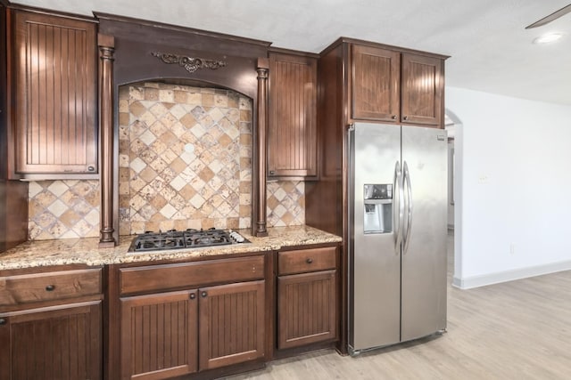 kitchen with light wood finished floors, decorative backsplash, appliances with stainless steel finishes, light stone countertops, and baseboards