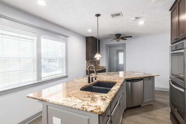 kitchen with stainless steel appliances, dark wood-style flooring, a sink, visible vents, and an island with sink