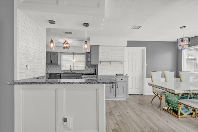 kitchen featuring decorative backsplash, gray cabinets, visible vents, light wood-type flooring, and a sink