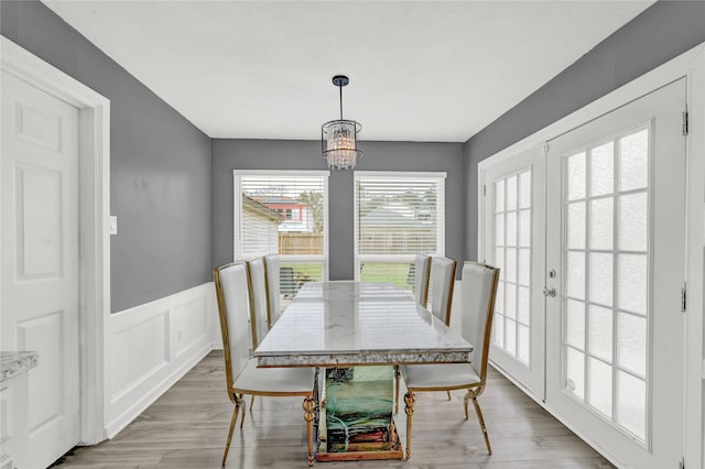 dining area featuring french doors, wainscoting, an inviting chandelier, a decorative wall, and light wood-style flooring
