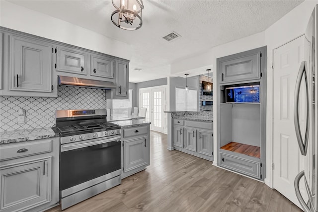 kitchen featuring visible vents, gray cabinets, under cabinet range hood, tasteful backsplash, and stainless steel appliances