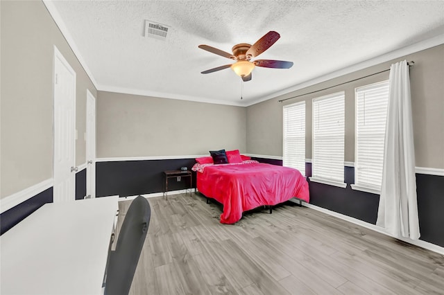 bedroom featuring a ceiling fan, a textured ceiling, visible vents, wood finished floors, and ornamental molding